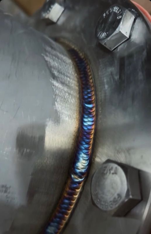 TIG cap with peacock heat tint on a bolted flange — stacked dimes, clean tie-in